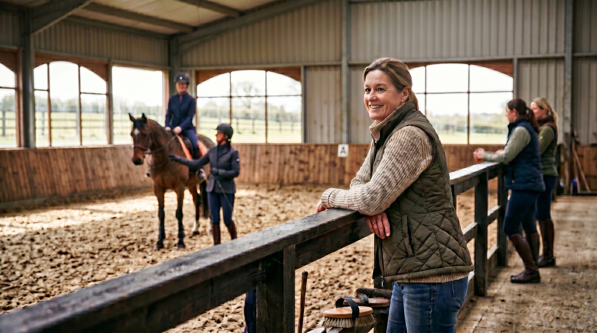 Barn mom standing at the rail watching a riding lesson with a supportive expression